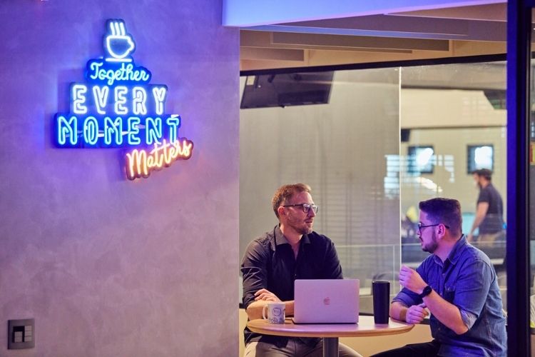 Homens de negócio sentados em uma mesa, com uma xícara de café e um notebook.