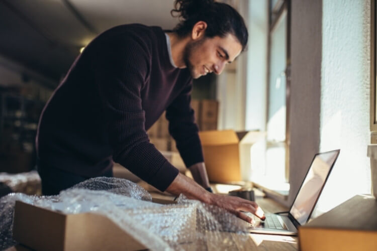 Homem mexendo em computador com caixas de papelão ao redor.