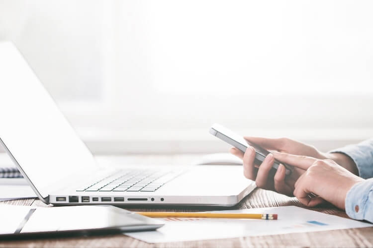 Homem mexendo no celular, com notebook em sua frente.