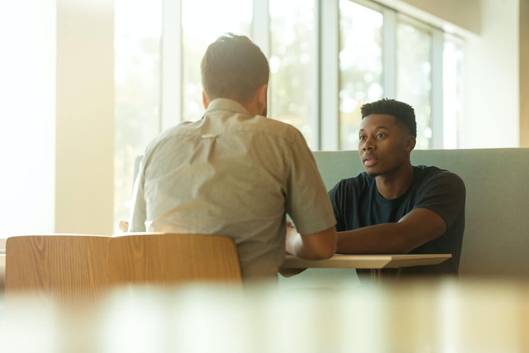 Homens conversando em mesa de trabalho.