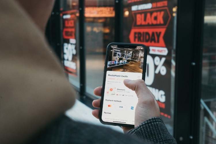 Pessoa mexendo no celular em frente a uma promoção de Black Friday.