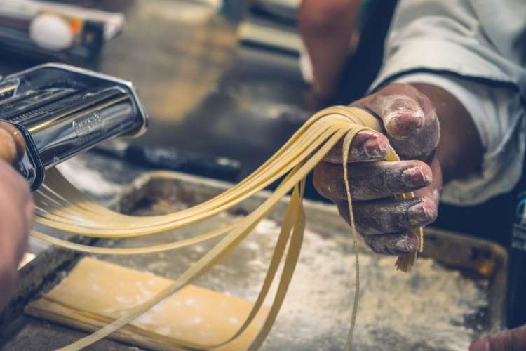 Cozinheiro passando massa de macarrão no rolo.