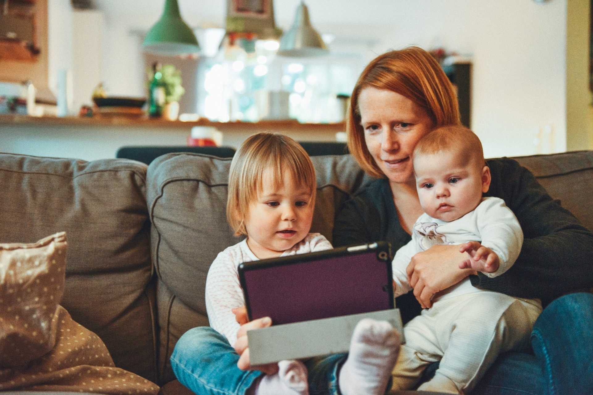 Mãe com seus filhos no colo, mexendo em um tablet.