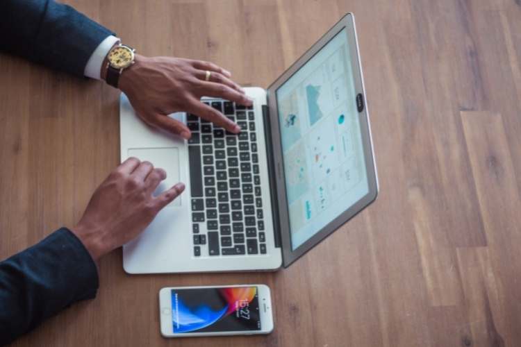 Homem de terno mexendo no computador, com celular ao lado.