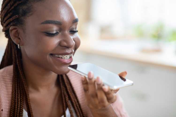 Mulher negra sorrindo e dando comando de voz para celular.