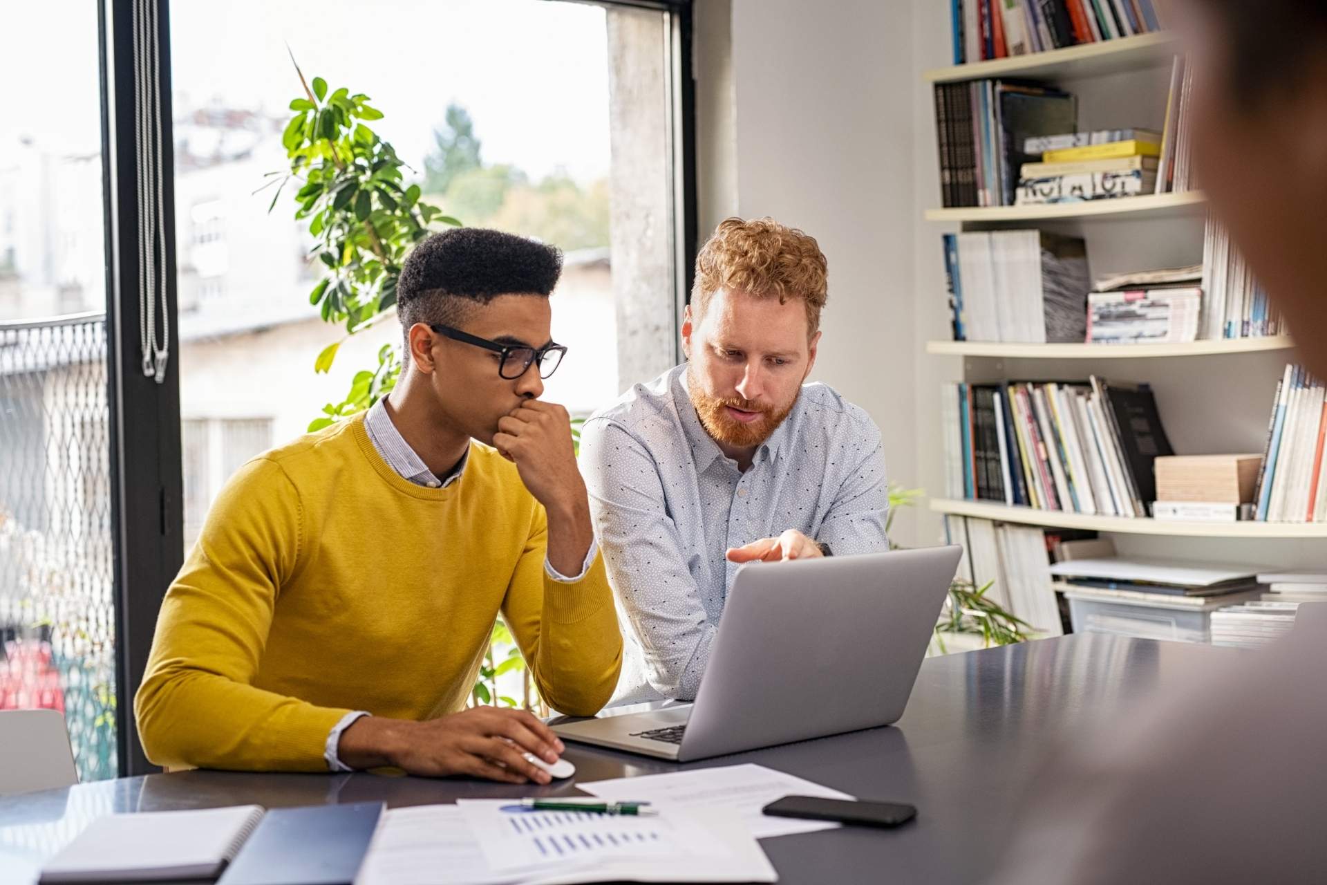 Homens com roupas sociais olhando para o notebook com expressão séria.