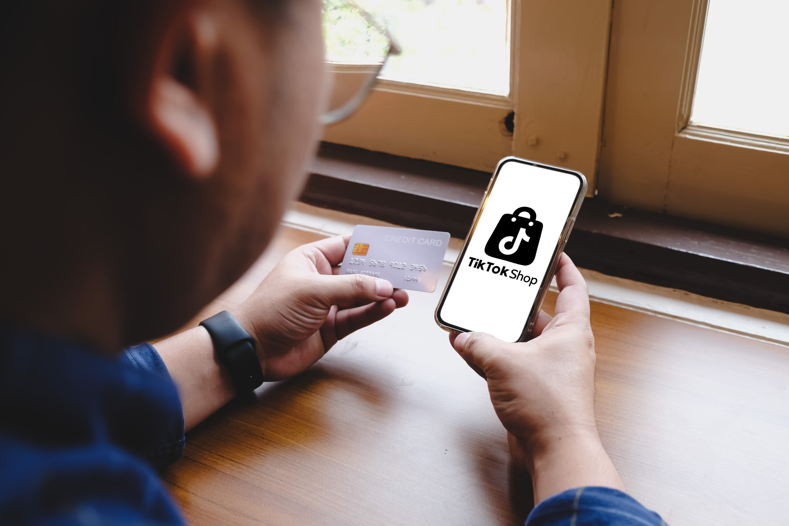 Homem sentado mexendo no celular com a aba do TikTok Shop aberta.