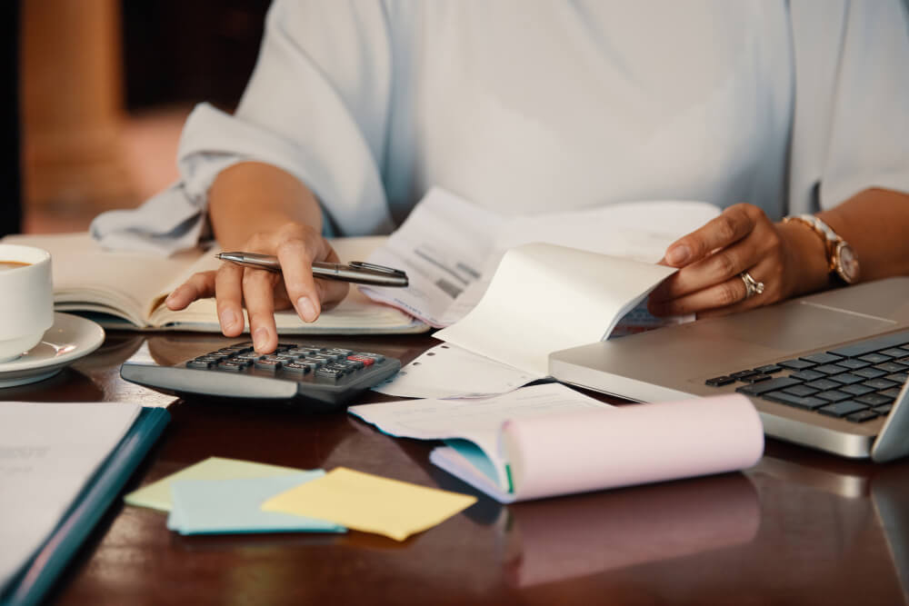 Profissional faz contas com calculadora e documentos sobre a mesa, ilustrando o impacto da reforma tributária na gestão financeira.