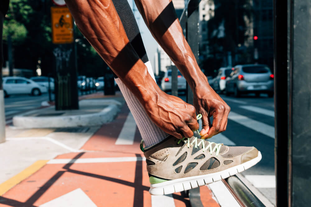 Homem amarra tênis de corrida em ambiente urbano, representando o foco esportivo do Netshoes marketplace.