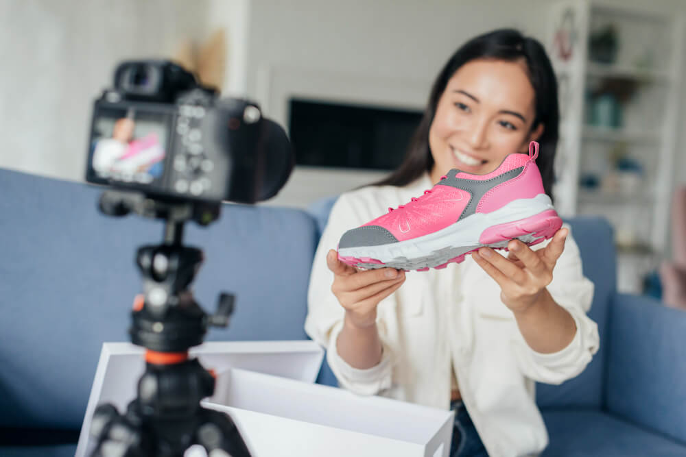 Influenciadora grava vídeo mostrando tênis esportivo rosa, simbolizando vendas online no Netshoes marketplace.