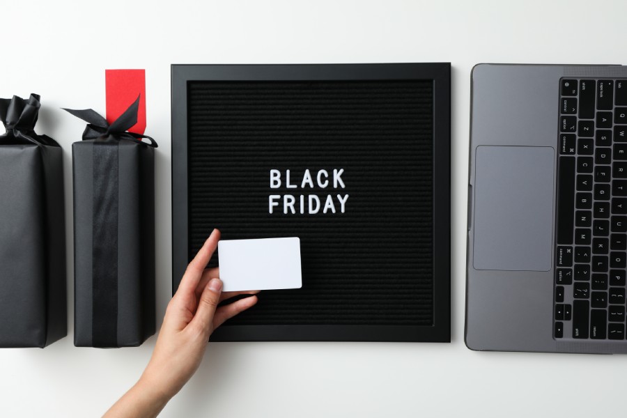 Mão com cartão branco, quadro 'Black Friday', notebook e sacolas