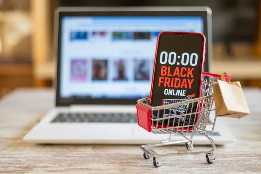 Carrinho miniatura com smartphone em contagem regressiva para Black Friday no e-commerce e notebook ao fundo.