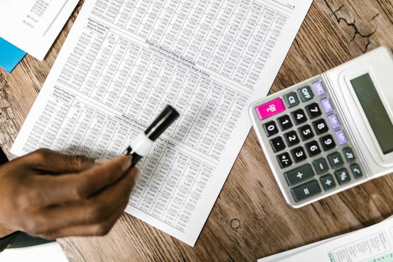 Pessoa analisando planilha financeira com caneta e calculadora sobre a mesa, representando o cálculo da elasticidade de preços e a relação entre preço e demanda.