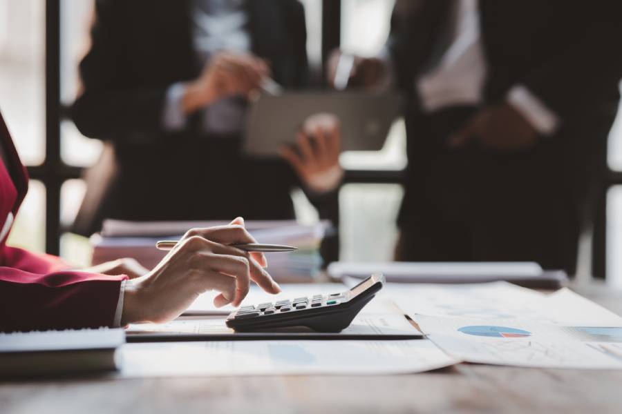 Pessoa calculando valores com relatórios e equipe ao fundo, simbolizando gestão e split payment.