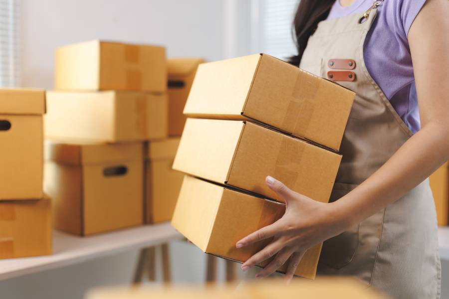 Funcionária transportando caixas em centro de distribuição da logística da Amazon para envio de pedidos.
