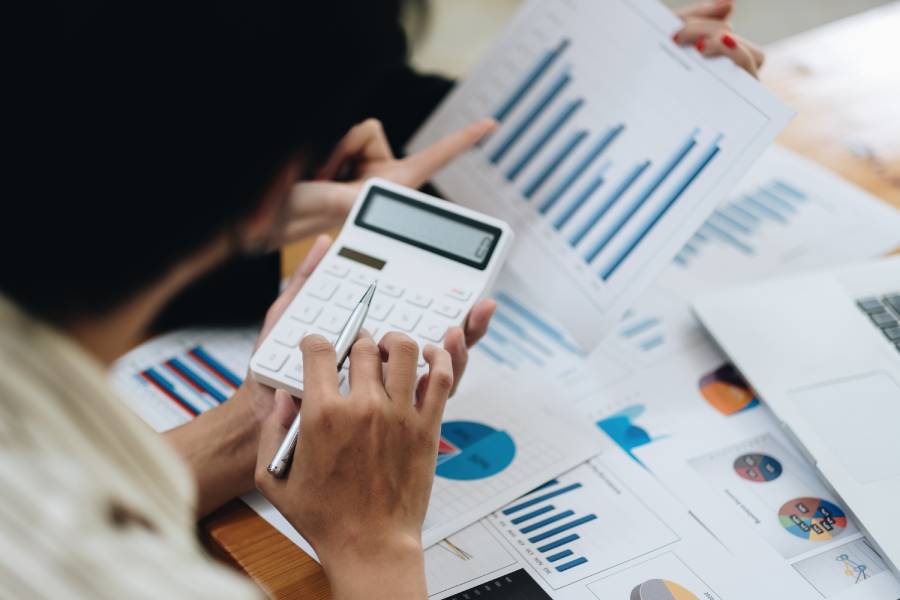 Pessoa usando calculadora e analisando relatórios com gráficos de barras e pizza impressos sobre uma mesa, durante o planejamento de campanhas da Amazon