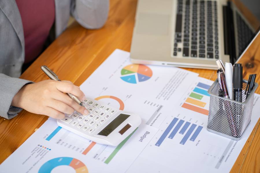 Mãos usando calculadora sobre relatórios com gráficos para análise de DRE e controle de budget