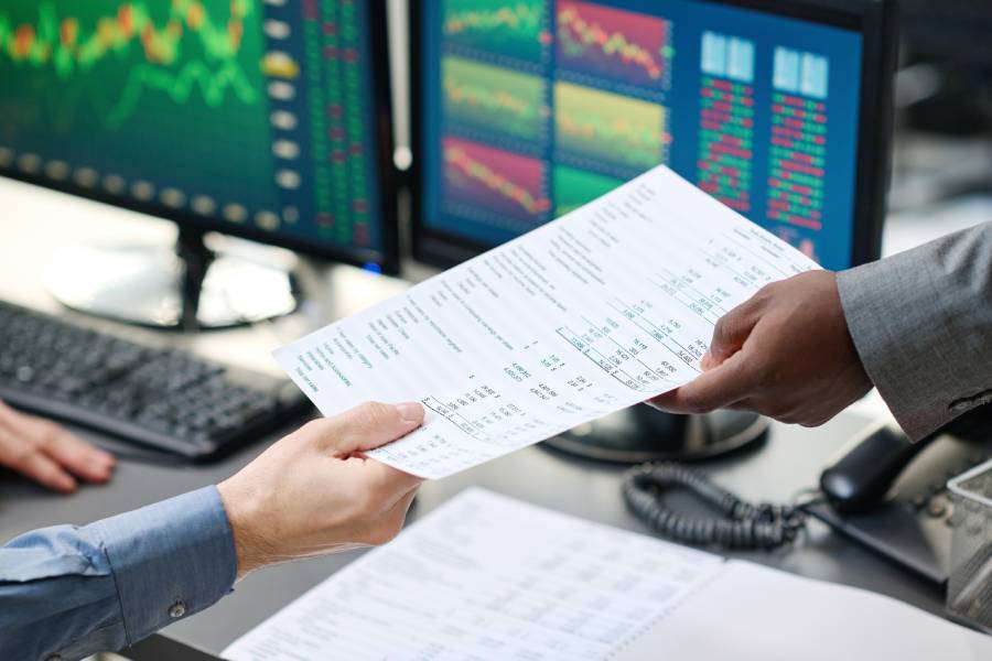 Profissionais analisando relatório de antecipação de recebíveis com gráficos financeiros ao fundo