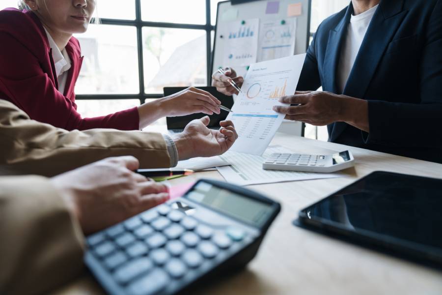 Profissionais em reunião revisando relatórios e calculadora, ilustrando conciliação bancária.