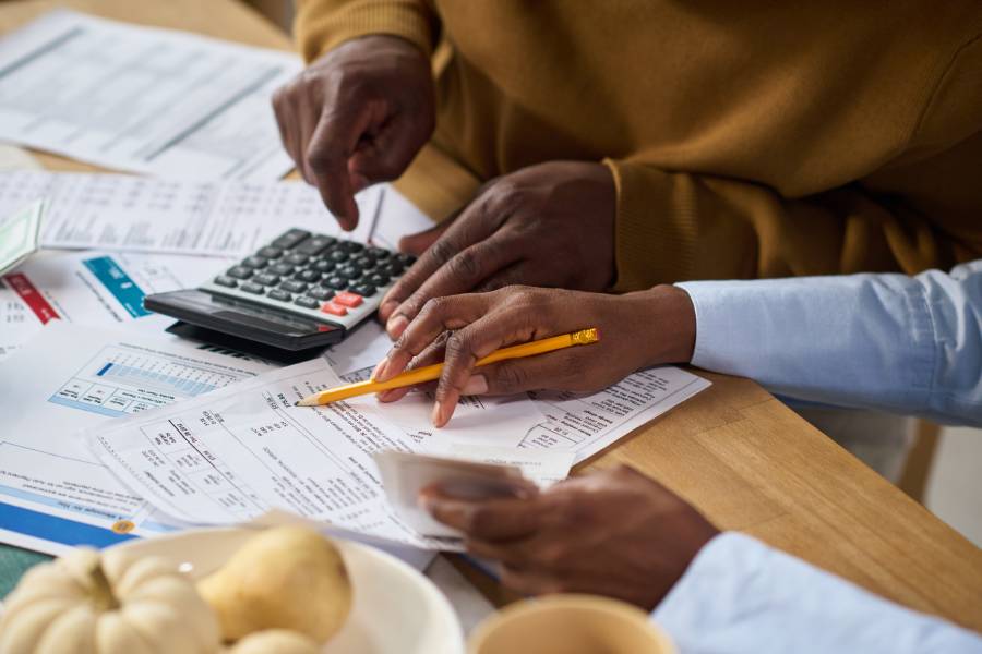 Duas pessoas analisando documentos financeiros e usando calculadora para fazer a conciliação do Mercado Livre