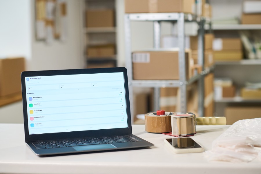 Laptop com sistema de gestão aberto em armazém com prateleiras, ilustrando hub de integração marketplace em uso