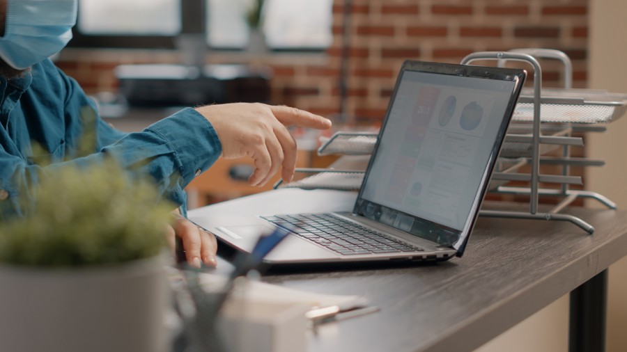 Pessoa apontando para gráficos em laptop no escritório, mostrando o impacto do CNPJ Alfanumérico