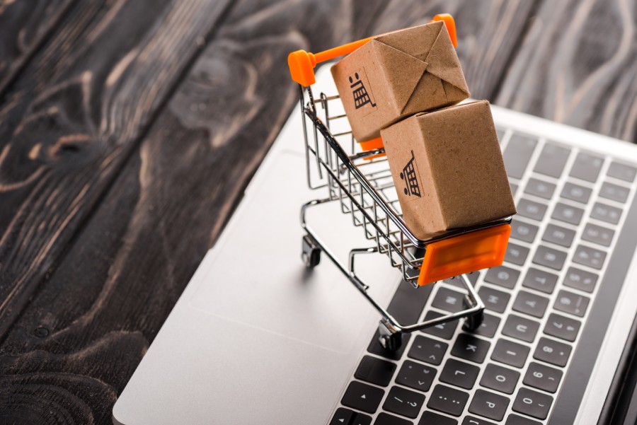 Mini carrinho de compras laranja com caixas de papelão sobre um notebook, ilustrando vendas e o repasse Shopee
